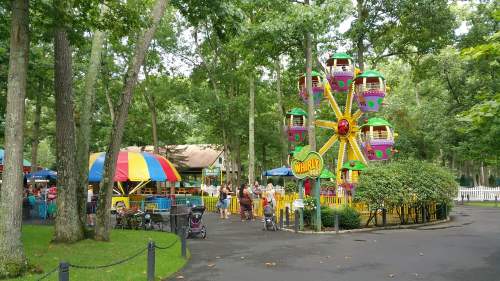 A colorful amusement park with a Ferris wheel and a carousel, surrounded by trees and families enjoying the day.