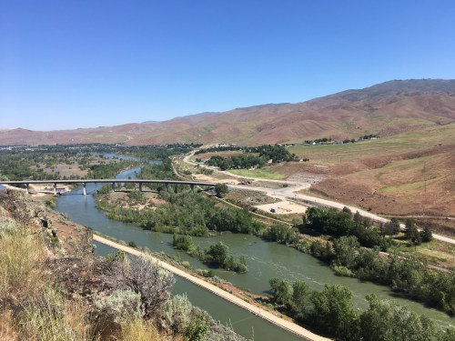 A scenic view of a river winding through green trees and hills under a clear blue sky.