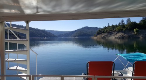 View of a calm lake surrounded by mountains, with a spiral staircase and chairs in the foreground.