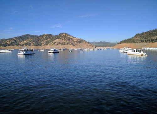 A serene lake scene with several boats floating on calm water, surrounded by hills under a clear blue sky.