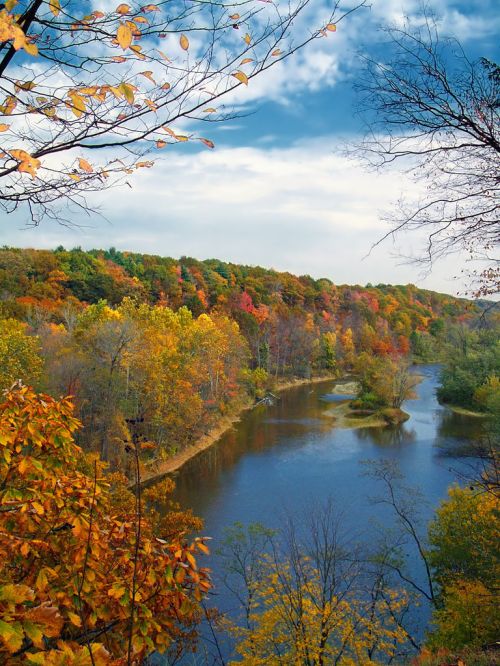A serene river flows through a vibrant autumn landscape with colorful trees under a blue sky.