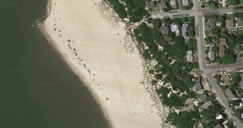 Aerial view of a sandy beach with scattered umbrellas and a nearby residential area.