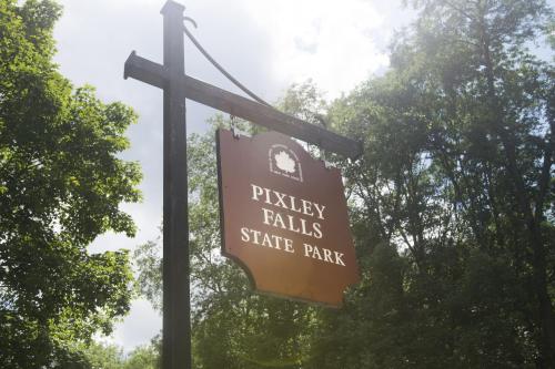 Sign for Pixley Falls State Park surrounded by trees under a cloudy sky.