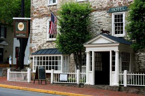 Historic stone building with a sign for "Red Fox Inn," featuring an American flag and a black cat on the roof.
