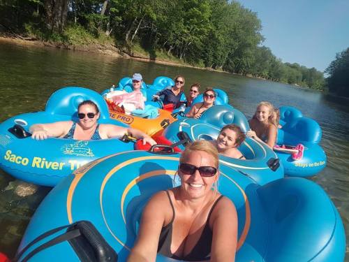 A group of eight people enjoying a sunny day floating on colorful inner tubes in a river surrounded by trees.
