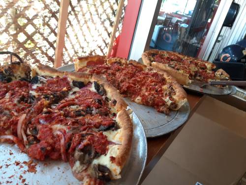 Three pizzas on metal trays, topped with sauce, cheese, and various toppings, sitting on a table with a lattice background.