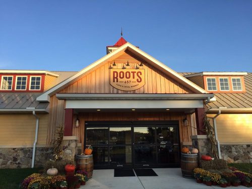 Exterior of a rustic building with a sign reading "ROOTS 657," surrounded by pumpkins and autumn decorations.