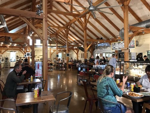 A spacious, rustic restaurant interior with wooden beams, tables, and patrons enjoying meals and drinks.