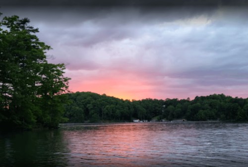 A serene lake at sunset, with vibrant pink and purple skies and lush green trees along the shore.