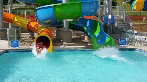 A colorful water slide at a pool, with a person sliding down and splashing into the water below.