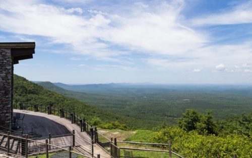 A scenic view from a mountain overlook, featuring lush green valleys and a blue sky with scattered clouds.