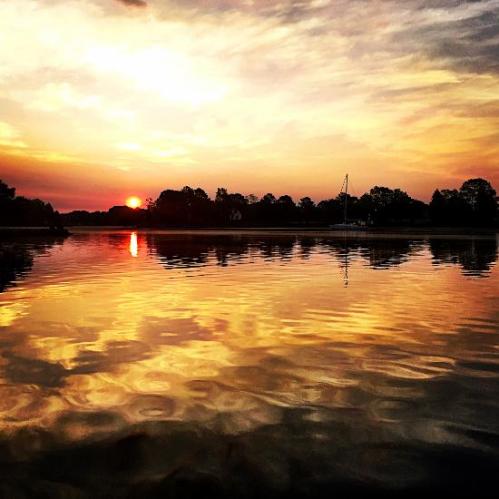 A serene sunset over a calm lake, with vibrant orange and yellow reflections on the water's surface.