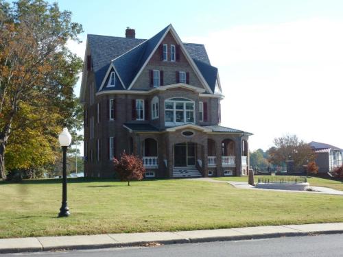 A large, historic brick house with a steep roof, white trim, and a spacious lawn, set against a clear blue sky.