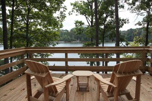 A serene lakeside view from a wooden deck with two chairs and a small table surrounded by trees.