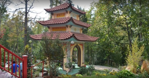 A decorative pagoda surrounded by trees and greenery, with a pathway leading up to it.