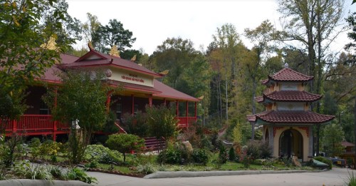 A serene landscape featuring a red-roofed building and a traditional pagoda surrounded by lush greenery.