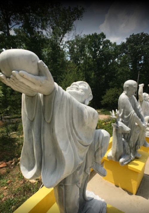 A row of white stone statues depicting figures in traditional attire, set against a green background.