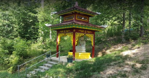 A colorful gazebo with intricate designs, surrounded by lush greenery and steps leading up to it.