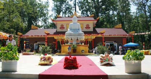 A serene Buddhist temple with a large statue of Buddha, flanked by colorful lion dance costumes and lush greenery.