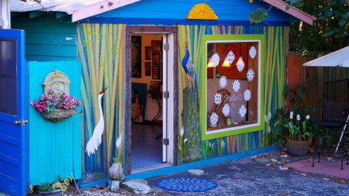 Colorful cottage with vibrant murals of birds and plants, featuring an open door and a decorative window.