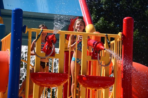 Two children play on a colorful water slide structure, spraying water and enjoying a sunny day at a water park.
