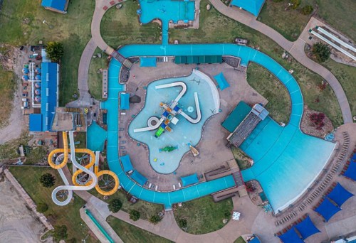 Aerial view of a water park featuring pools, slides, and lounging areas surrounded by green grass.