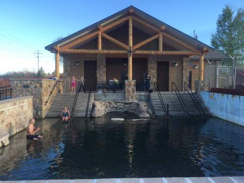 A rustic building with wooden beams overlooks a natural pool, where two people relax in the water.