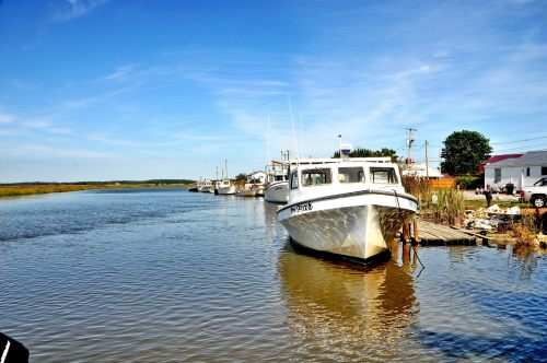 A calm waterway with boats docked along the shore under a clear blue sky.