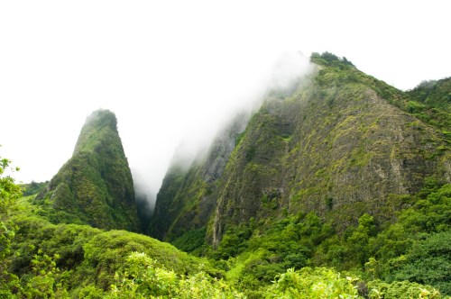Two towering green mountains shrouded in mist, surrounded by lush vegetation.
