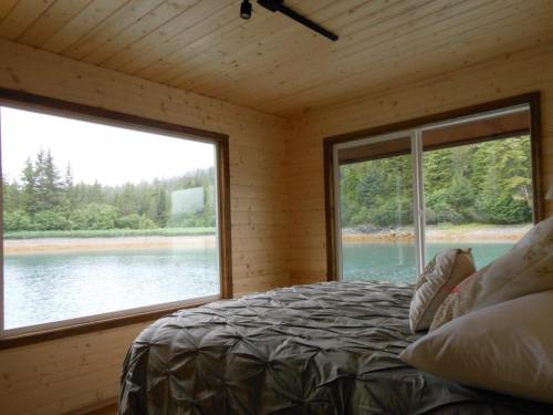 Cozy bedroom with a view of a serene lake and forest through large windows. Natural wood interior.