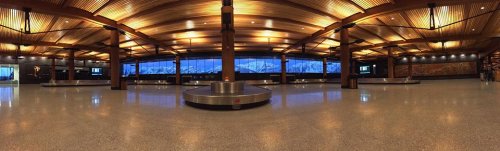A spacious airport baggage claim area with wooden ceilings and large windows showcasing mountain views.