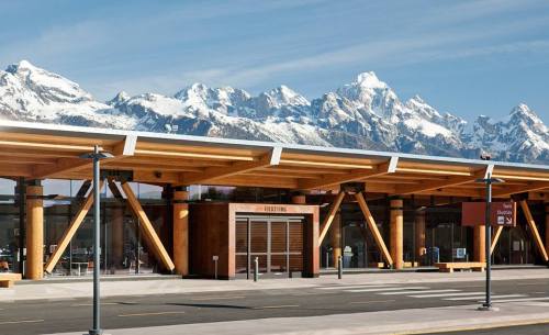 Modern building with wooden architecture, set against a backdrop of snow-capped mountains under a clear blue sky.