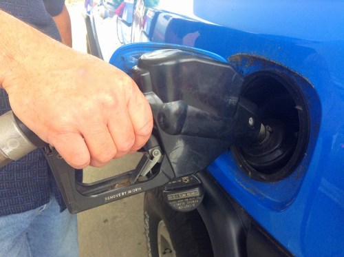 A hand holding a fuel nozzle while refueling a blue vehicle at a gas station.