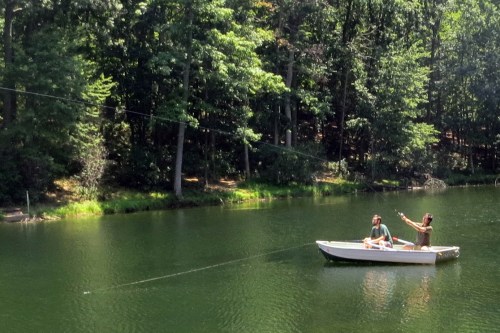 Two people in a small boat on a serene lake, surrounded by lush green trees.