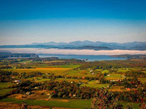 A scenic view of rolling hills, a lake, and mountains under a clear blue sky with fog in the valley.