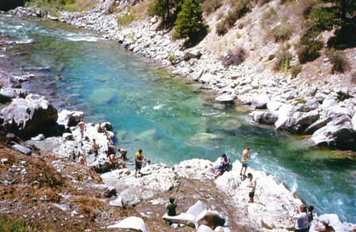 A scenic river surrounded by rocky banks, with people enjoying the water and sun on a warm day.