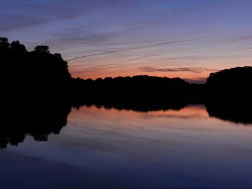 A serene lake at sunset, reflecting colorful skies and silhouettes of trees along the shore.