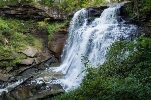 A cascading waterfall surrounded by lush greenery and rocky terrain, creating a serene natural landscape.