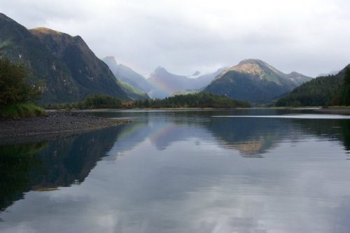 A serene landscape featuring mountains reflected in a calm lake, with a hint of a rainbow in the background.