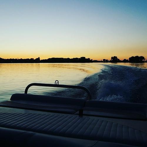 A boat glides over calm water at sunset, with trees silhouetted against the colorful sky.