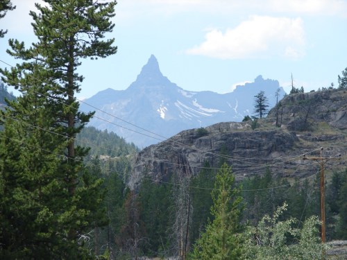 A scenic view of rugged mountains in the background, framed by trees and power lines in the foreground.