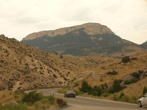 A winding road through arid landscape with a large mountain in the background under a cloudy sky.