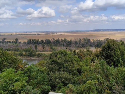A scenic view of a vast landscape with fields, trees, and a river under a partly cloudy sky.