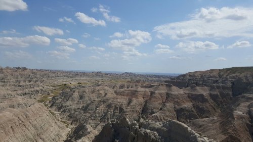 A panoramic view of rugged, layered rock formations under a blue sky with scattered clouds.
