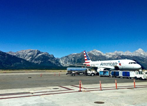 An American Airlines plane at an airport with mountains in the background under a clear blue sky.