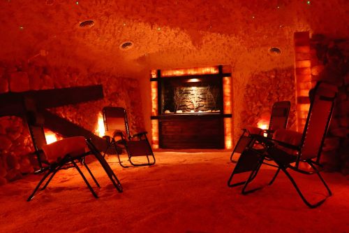 A tranquil salt room with glowing salt walls, reclining chairs, and a calming water feature in the center.