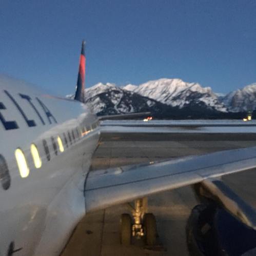 A Delta airplane on the runway with snow-capped mountains in the background during twilight.