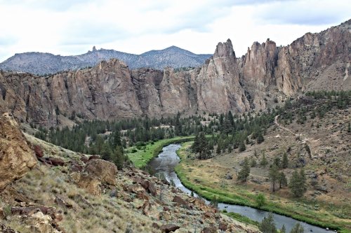 A scenic view of rugged cliffs and a winding river surrounded by green vegetation and mountains under a cloudy sky.