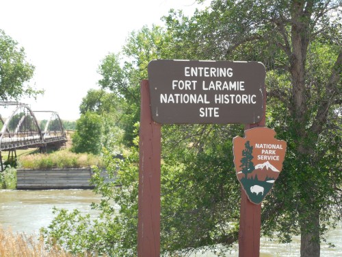 Sign marking the entrance to Fort Laramie National Historic Site, with a river and trees in the background.