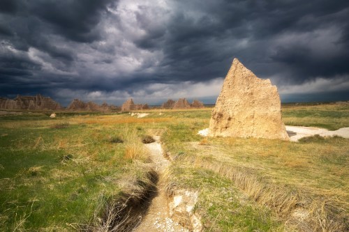 A rugged rock formation stands in a grassy landscape under a dramatic, cloudy sky.